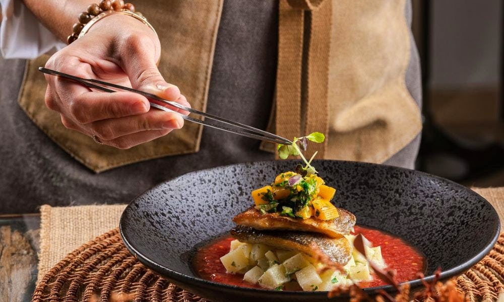 A chef putting food onto a plate with tweezers