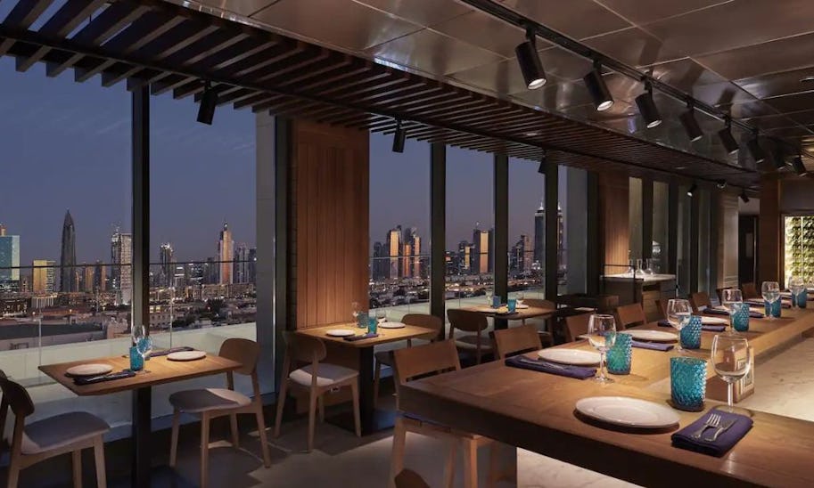 A simply dressed dining room with wooden tables and chairs looking over Dubai