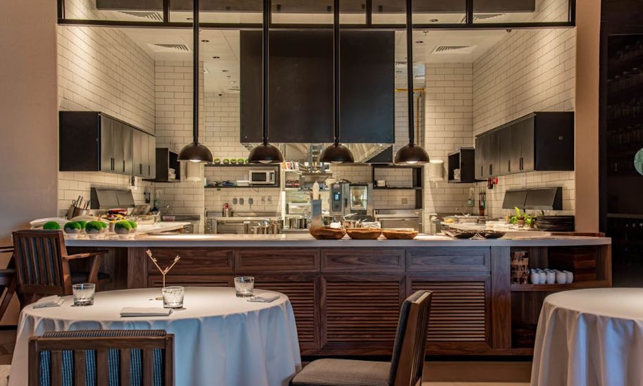 An open kitchen with white tiled walls as seen from the dining room