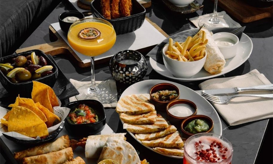A table laid with multiple plates of sharing food and cocktails
