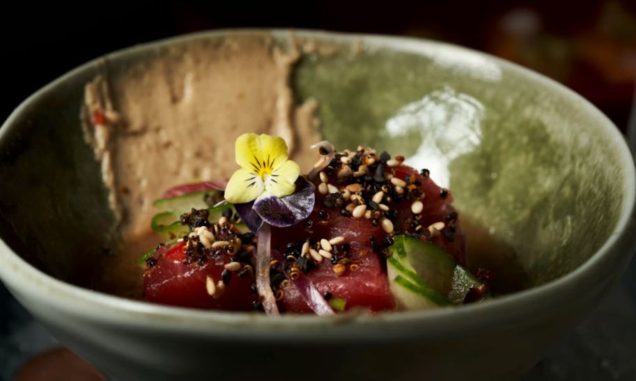 A bowl of chopped tuna sashimi topped with edible flowers and sesame seeds