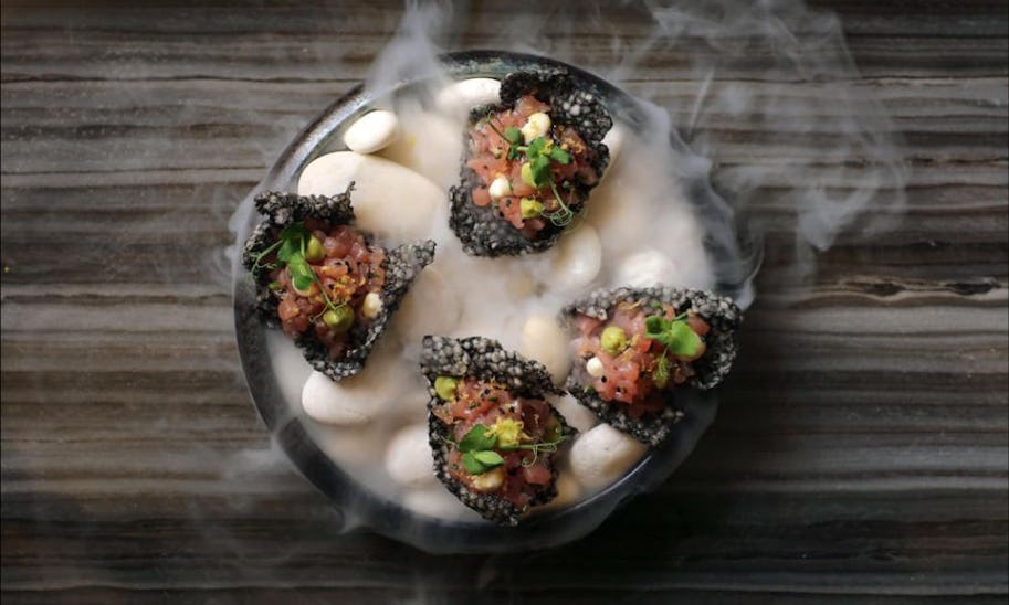 A plate filled with smoke from dry ice with some tuna canapes on top