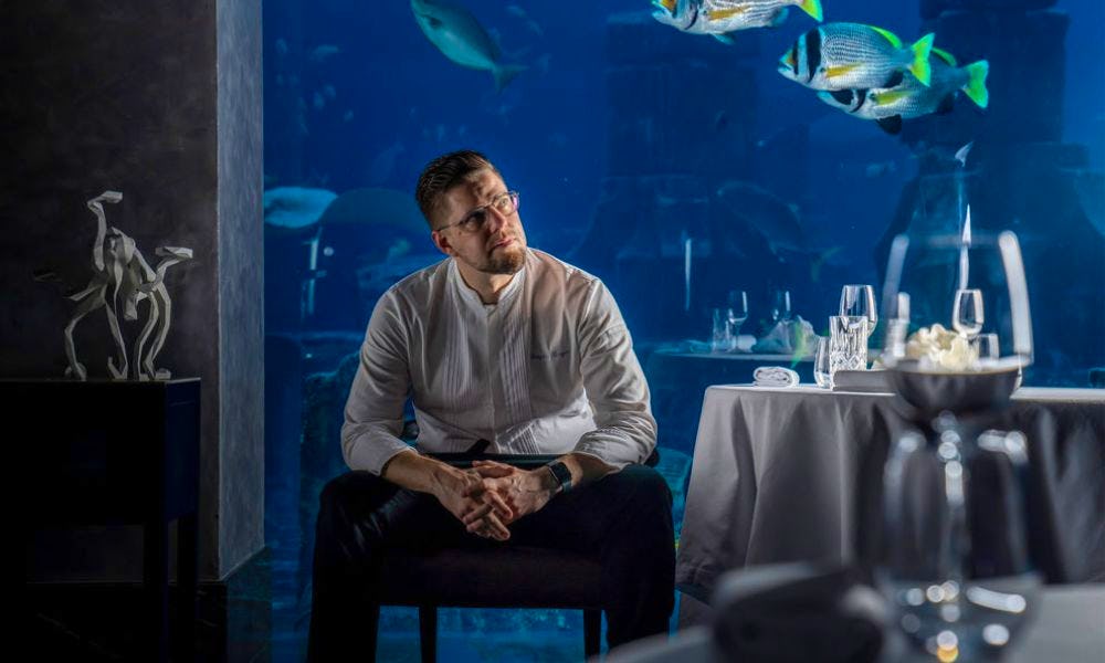 A man sitting alone at a table with a view of a aquarium
