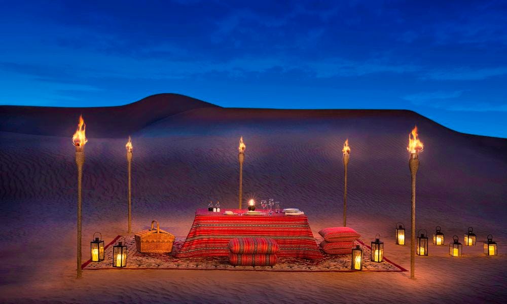 A private dining set-up in the desert at dusk, on a rug surrounded by candles