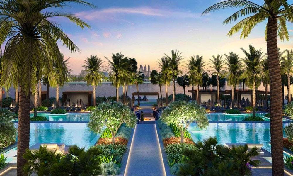 Two palm-fringed swimming pools with a walkway between them and the sea ahead